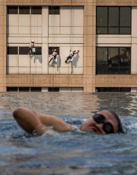 Group of workers cleaning windows service on high rise office building with reflection from swimming pool. Selective focus.