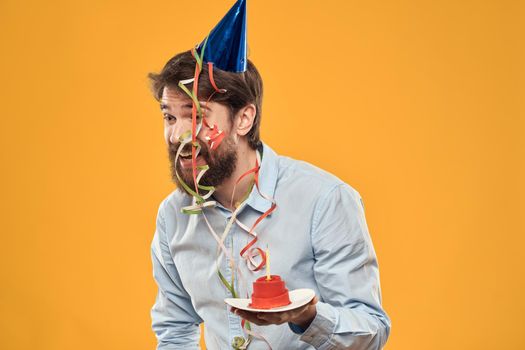 Cheerful man with a cake on a yellow background birthday holidays cap on his head. High quality photo