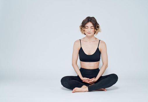 A woman is meditating on a light background with her legs crossed on the floor. High quality photo