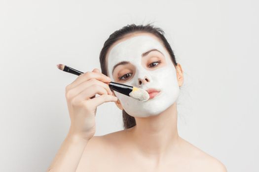 woman with bare shoulders face cream makeup brush in hand. High quality photo