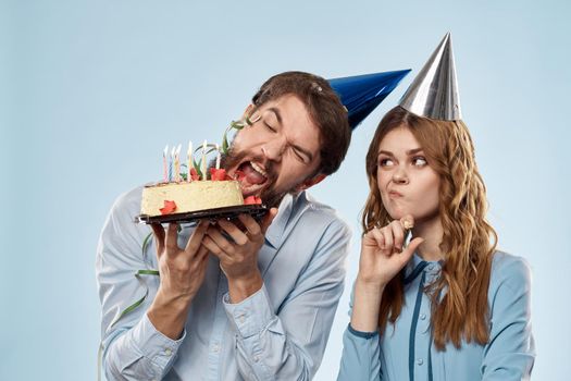 Birthday man woman in party hats on a blue background and cake with candles. High quality photo