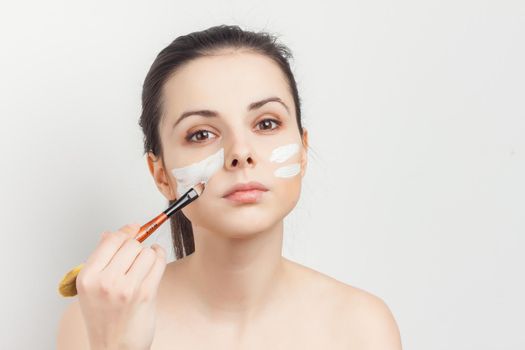 woman with bare shoulders face cream makeup brush in hand. High quality photo