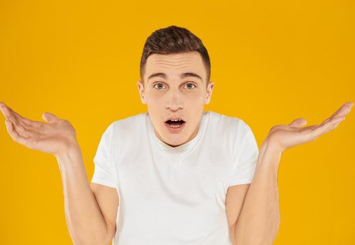 Emotional guy in a white T-shirt on a yellow background gestures with his hands portrait close-up beautiful face. High quality photo