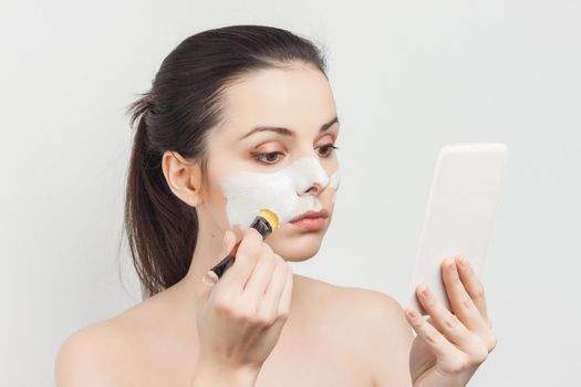 woman with bare shoulders face cream makeup brush in hand. High quality photo