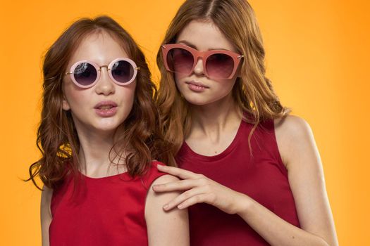 cheerful mom and daughter wearing sunglasses lifestyle friendship family yellow background studio. High quality photo