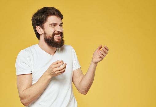 A man with a bushy beard on a yellow background gestures with his hands. High quality photo