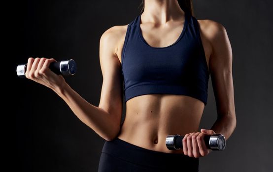woman with pumped up abdominal muscles holds a dumbbell in her hand on a dark background. High quality photo