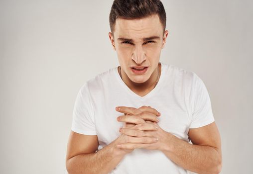 Guy in a white T-shirt sadness emotions model light background gesticulate with his hands. High quality photo