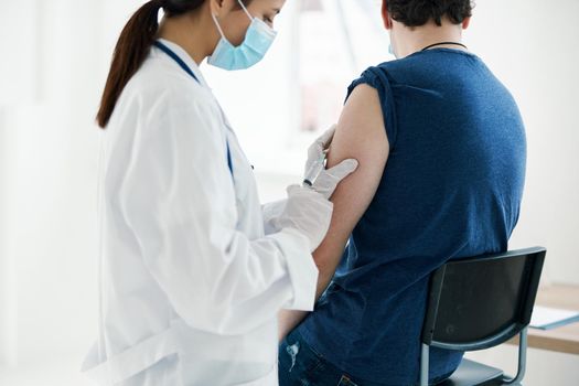 woman doctor in a medical mask injecting a man in a blue t-shirt. High quality photo