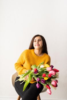 Beautiful young brunette in yellow sweater woman with bouquet of fresh pink tulips