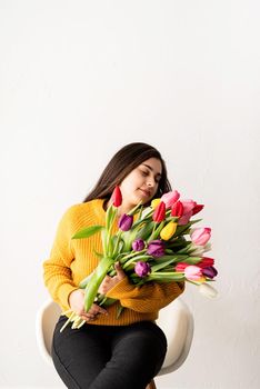 Beautiful young brunette in yellow sweater woman with bouquet of fresh pink tulips