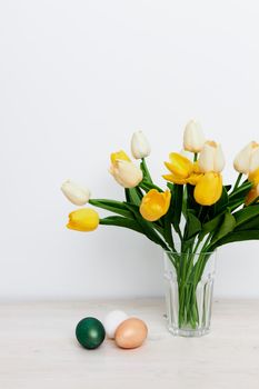 Yellow tulips in a vase and multi-colored eggs on the Easter table. High quality photo