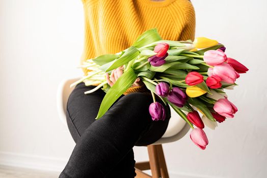 Beautiful young brunette in yellow sweater woman with bouquet of fresh pink tulips