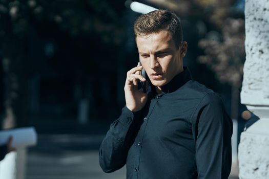 business man in a black shirt on the street talking on the phone. High quality photo