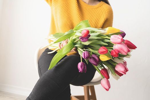 Beautiful young brunette in yellow sweater woman with bouquet of fresh pink tulips