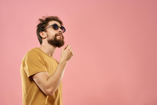Cute bearded man in a yellow T-shirt dark glasses pink background. High quality photo