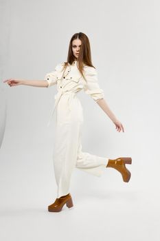 red-haired woman in overalls in brown boots is walking to the side on a light background. High quality photo