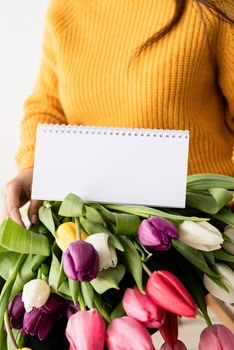 Beautiful young brunette woman in yellow sweater with bouquet of fresh pink tulips and blank calendar for mock up
