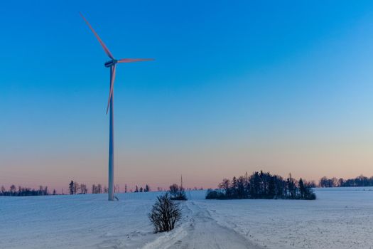 wind power plant in the field next to a power line at sunset.