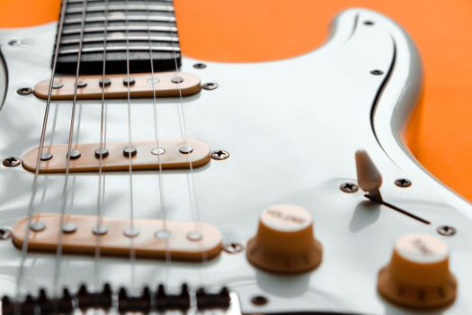 Detail of White Electric Guitar on a orange background.