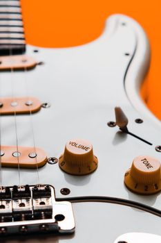 Detail of White Electric Guitar on a orange background.