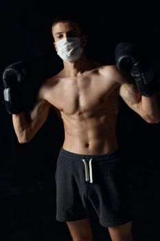 sporty man in medical mask and in boxing gloves on black background shorts fitness model press. High quality photo