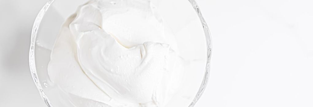 White whipped dessert cream served in a glass bowl, creamy texture closeup
