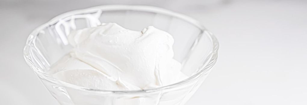 White whipped dessert cream served in a glass bowl, creamy texture closeup