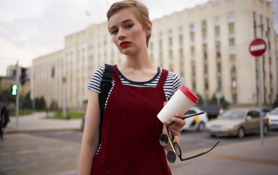 a woman in a sundress walks down the street with a cup of coffee in her hand. High quality photo