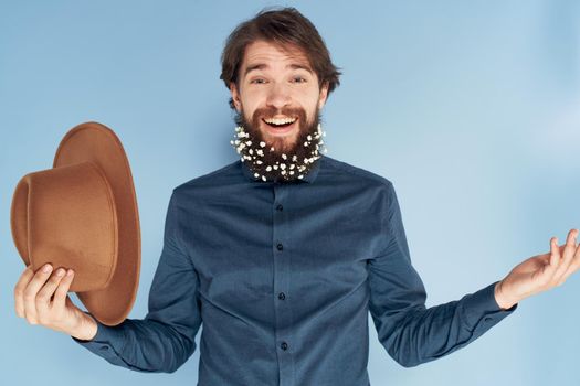 Cheerful man hat in hand beard with flowers emotions blue background. High quality photo