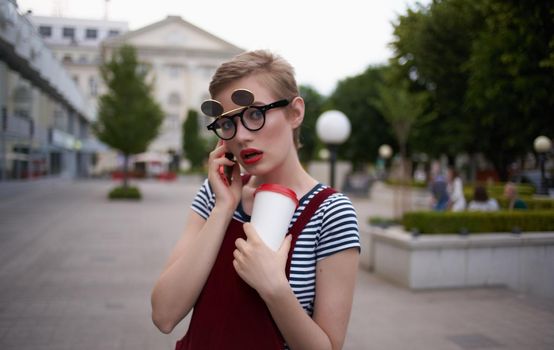 a woman in a sundress walks down the street with a cup of coffee in her hand. High quality photo