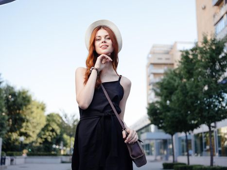 Pretty woman in a black T-shirt and hat are walking on the street near the building. High quality photo