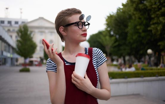 a woman in a sundress walks down the street with a cup of coffee in her hand. High quality photo