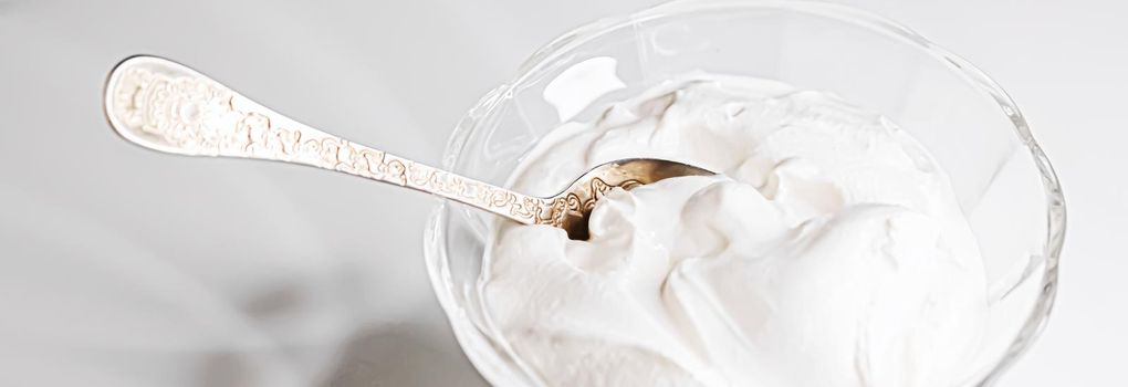 White whipped dessert cream served in a glass bowl, creamy texture closeup