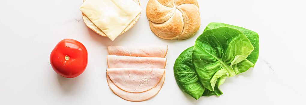 Food products and ingredients for making sandwich. Ham, cheese, burger bun, lettuce, cucumber and tomato as recipe flatlay on marble kitchen table background