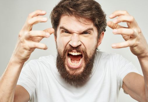 Aggressive man yells against a light background and gestures with his hands cropped view. High quality photo