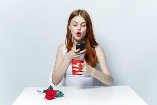 pretty woman sitting at a table with a phone in her hands emotions communication mug with a drink. High quality photo