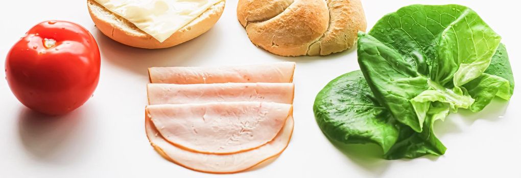 Food products and ingredients for making sandwich. Ham, cheese, burger bun, lettuce, cucumber and tomato as recipe flatlay on marble kitchen table background