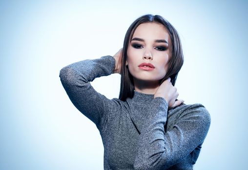Sexy brunette in a gray sweater on a light background holds her hands behind her head cropped view. High quality photo