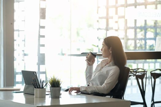 Portrait of beautiful woman or accountant sitting at desk in modern office with interior looking outside enjoying freetime