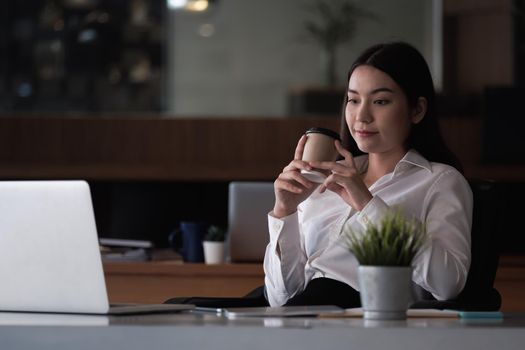 Portrait of young businesswoman looking at laptop screen while sitting at office desk in modern office.