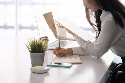 Photo of cheerful joyful asian woman writing down notes holding tablet for data analysis.