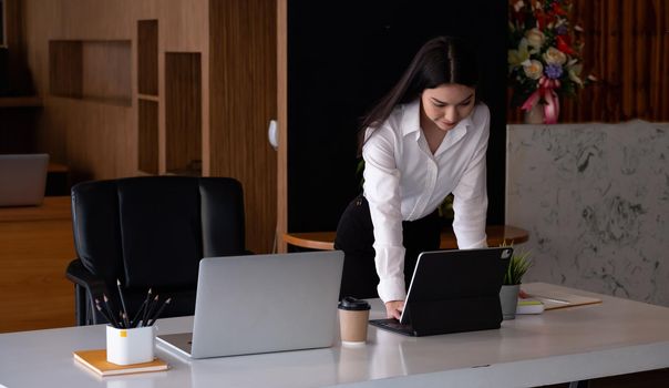 Charming asian businesswoman standing working on laptop on workspace in office.