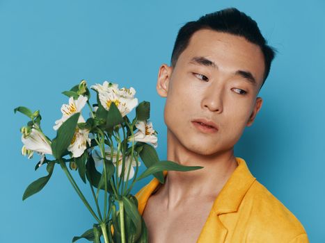 Handsome young man with a bouquet of white flowers on a blue background and Asian appearance. High quality photo