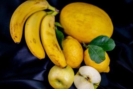 yellow fruit on a black background with melon bananas apples and lemons