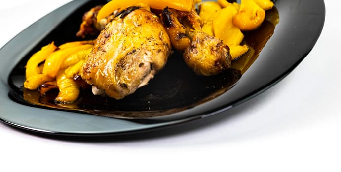 chicken so with yellow peppers on a black plate white background