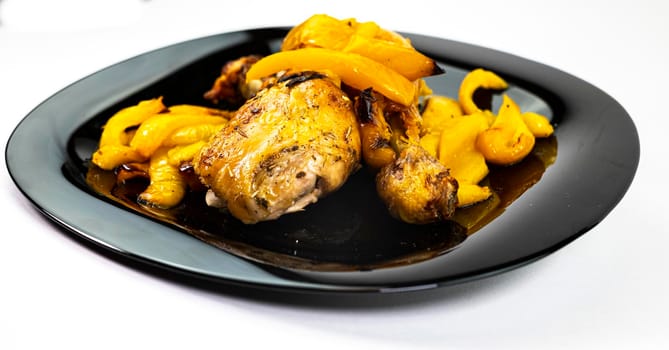 chicken so with yellow peppers on a black plate white background