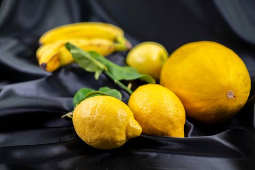 yellow fruit on a black background with melon bananas apples and lemons