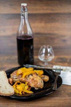 chicken legs and yellow peppers with glass bread and cutlery on black plate wood background