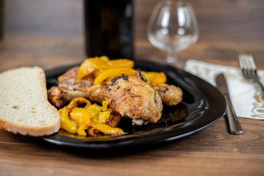 chicken legs and yellow peppers with glass bread and cutlery on black plate wood background